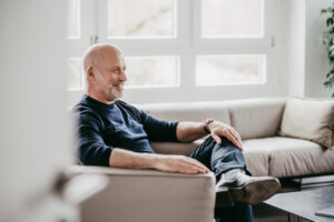 Das Bild zeigt Dr. Matthias Hallweger wie er lachend auf einem Sofa sitzt